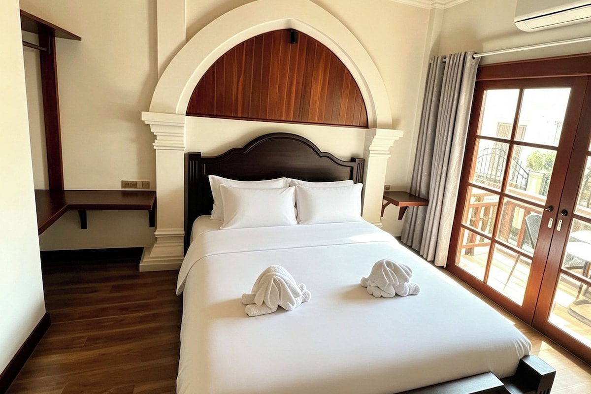 Une chambre d’hôtel avec un grand lit, un plafond en bois et une vue sur l’extérieur, visible à travers une porte vitrée.