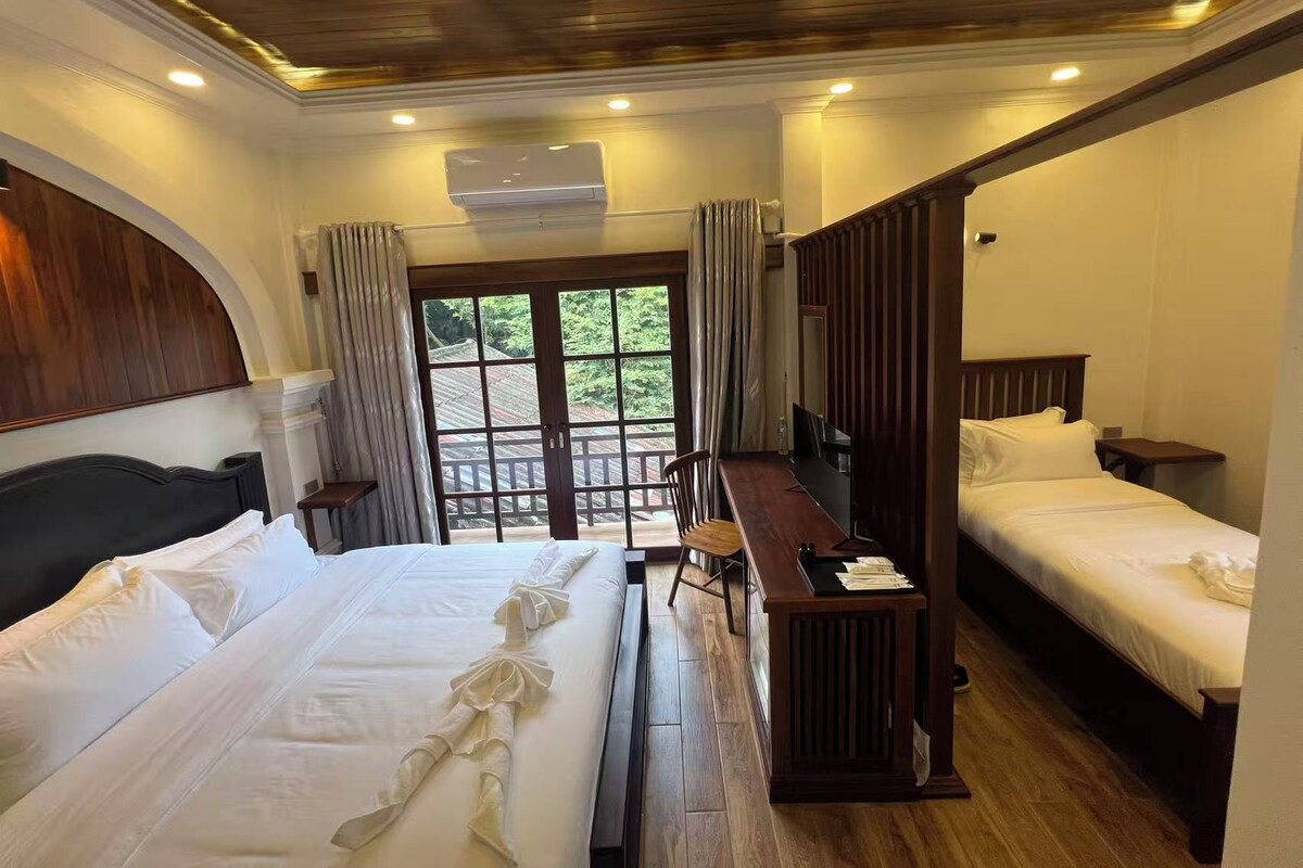 Une chambre d’hôtel avec deux lits, un plafond en bois, une grande fenêtre avec des rideaux et un bureau en bois.