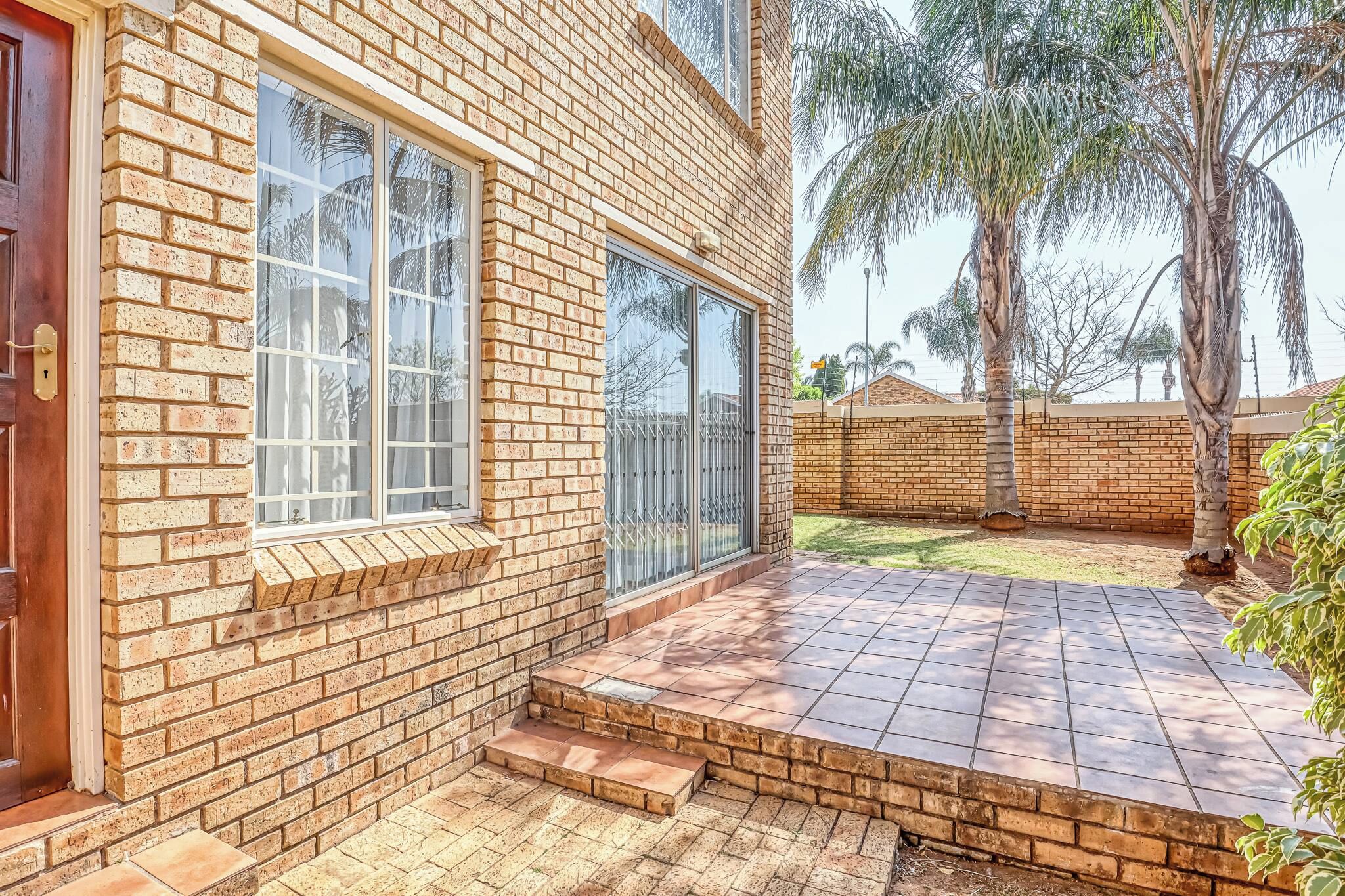 Una casa de ladrillo de dos pisos con puerta principal, ventanas amplias y un patio pavimentado.