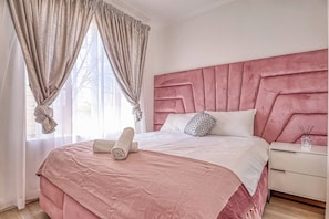 Une chambre à coucher avec un grand lit, une tête de lit, une table de chevet et une fenêtre avec des rideaux.