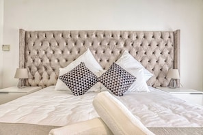 Uma cama com cabeceira estofada, duas almofadas estampadas e duas luminárias de mesa.