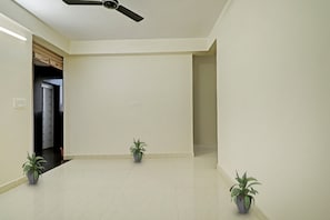 Habitació àmplia amb ventilador de sostre, dues plantes en test i una porta que condueix a una altra zona.
