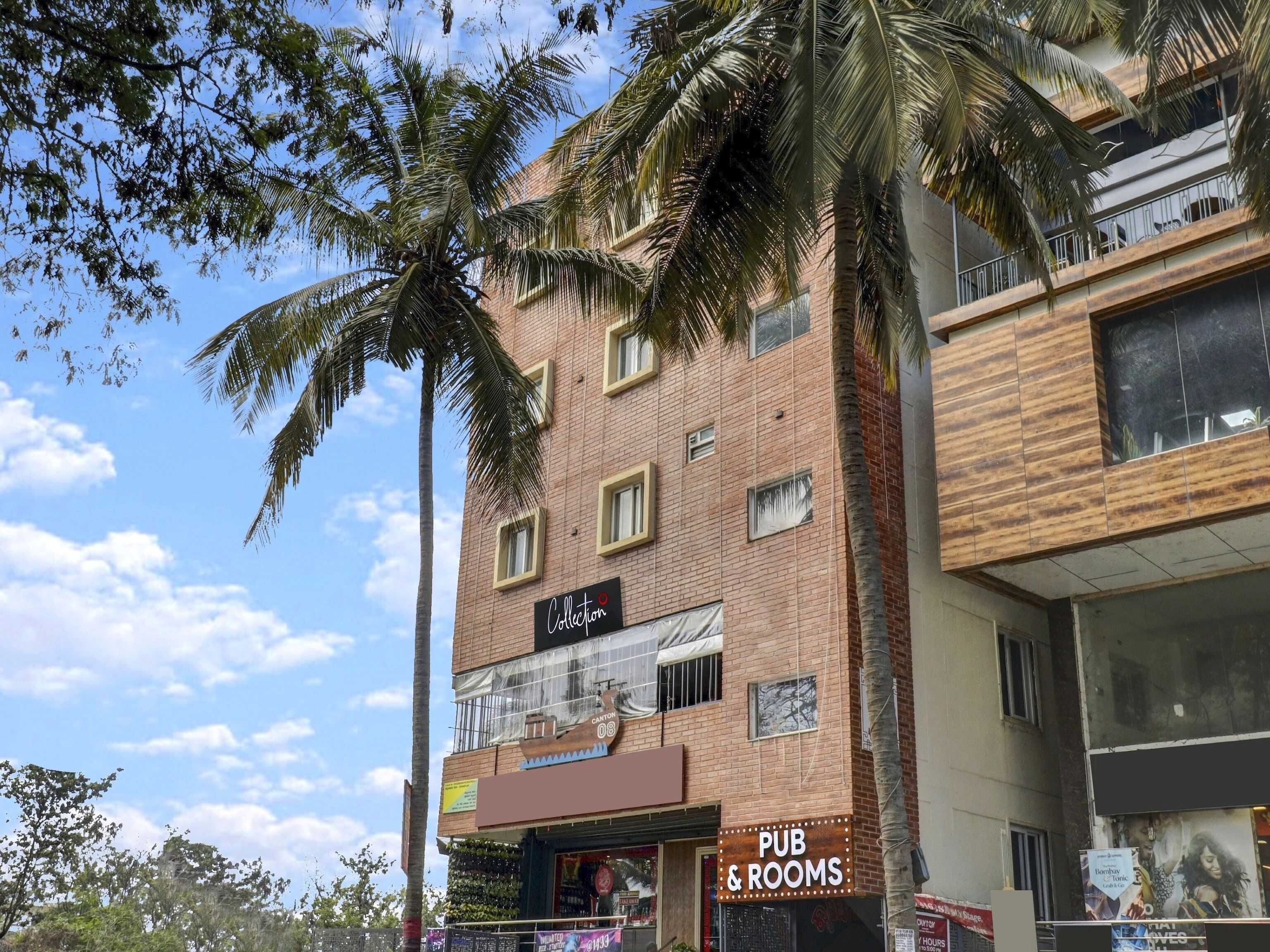 Un edificio de varios pisos con un pub y habitaciones en la planta baja, rodeado de palmeras y un cielo despejado.