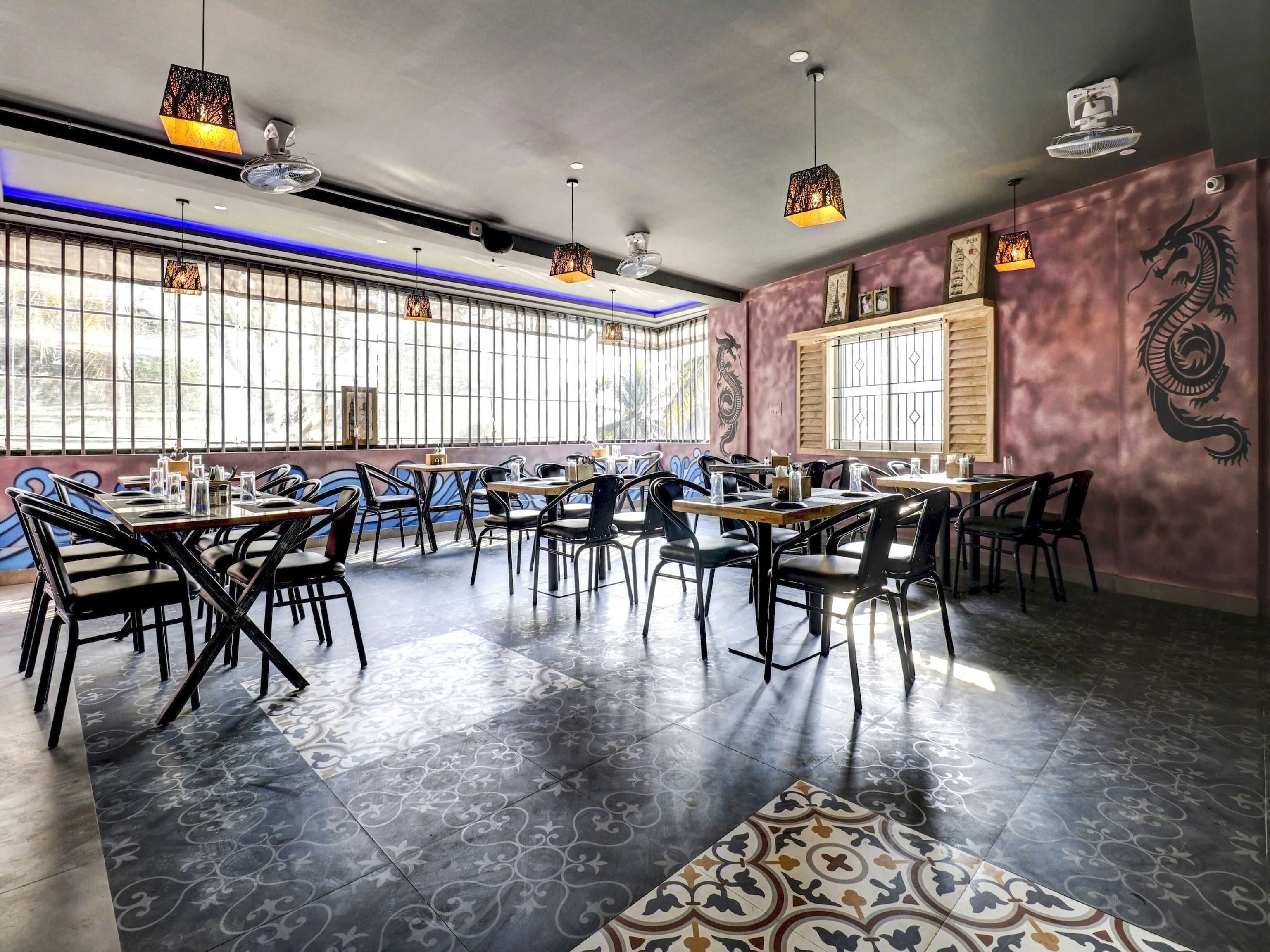 Un interior de restaurante con varias mesas y sillas, ventanas amplias y decoración artística en las paredes.