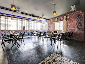 A restaurant interior with multiple tables and chairs, large windows, and decorative wall art. - Hotel O Canton (Bangalore)