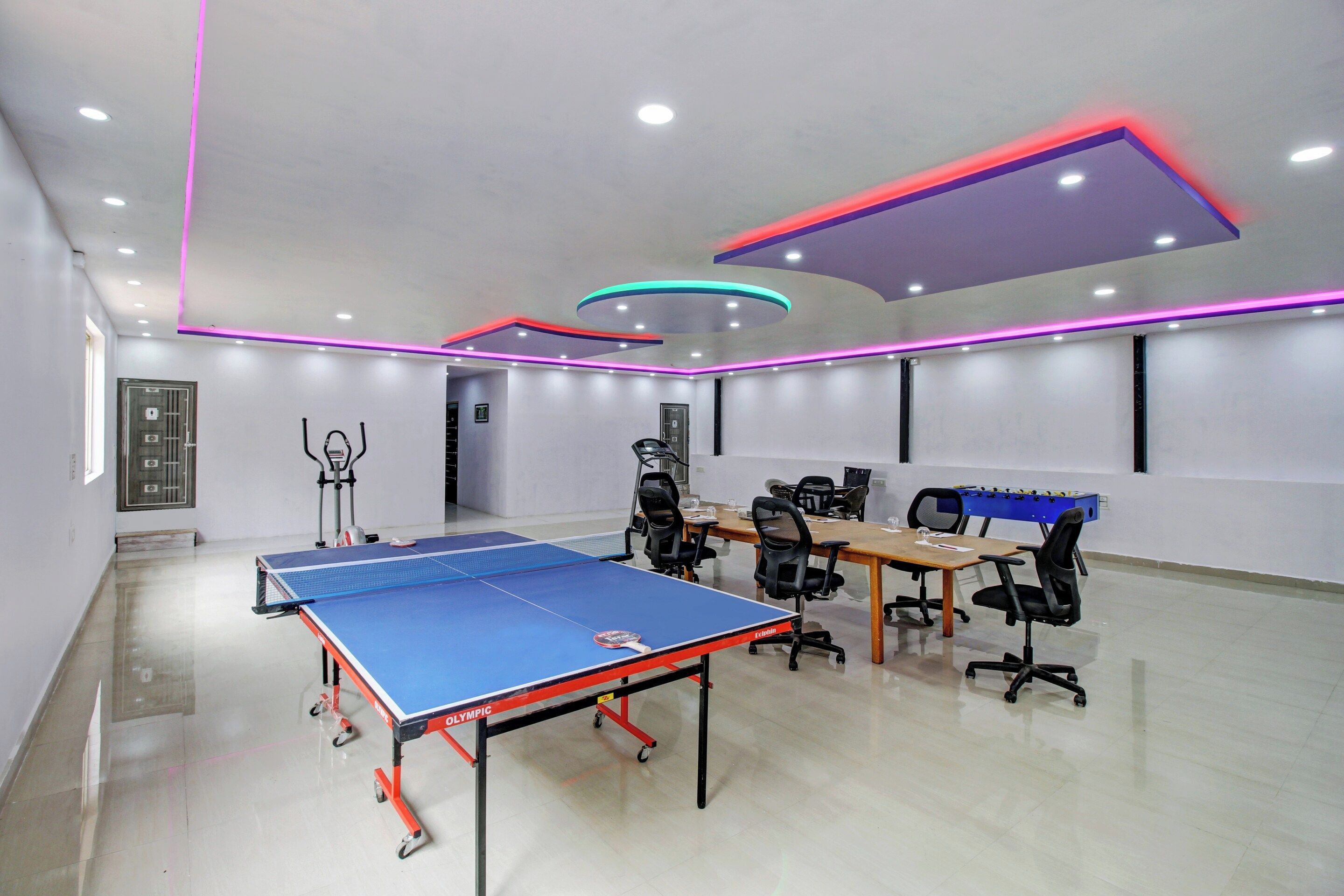Una habitación con mesa de ping pong, sillas de oficina, mesa de futbolín y cinta de correr.