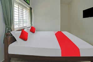 Una cama con ropa blanca y detalles rojos, un cabecero de madera y una ventana con cortinas.
