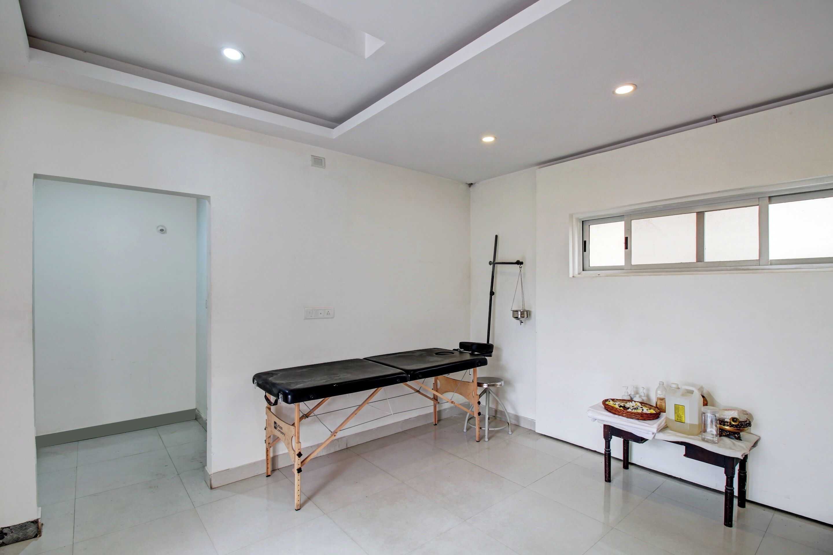 Una habitación con un banco de madera, una mesita con artículos de aseo y un ventanal.