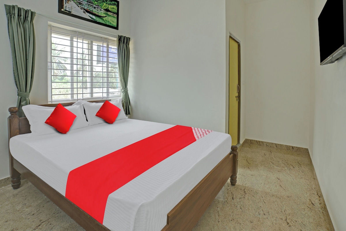 Una cama bien tendida con una colcha blanca y roja, dos almohadas rojas y un cabecero de madera.