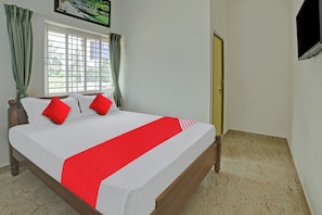 Una cama bien tendida con una colcha blanca y roja, dos almohadas rojas y un cabecero de madera.
