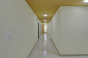 Un pasillo largo y estrecho con paredes blancas y piso de baldosas, que conduce a una puerta al final.