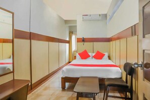 Habitación de hotel con cama, mesita de noche, silla, armario y equipo de aire acondicionado.