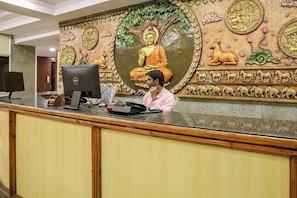 Una recepción con un computador, una persona sentada detrás y un gran mural de Buda en la pared.