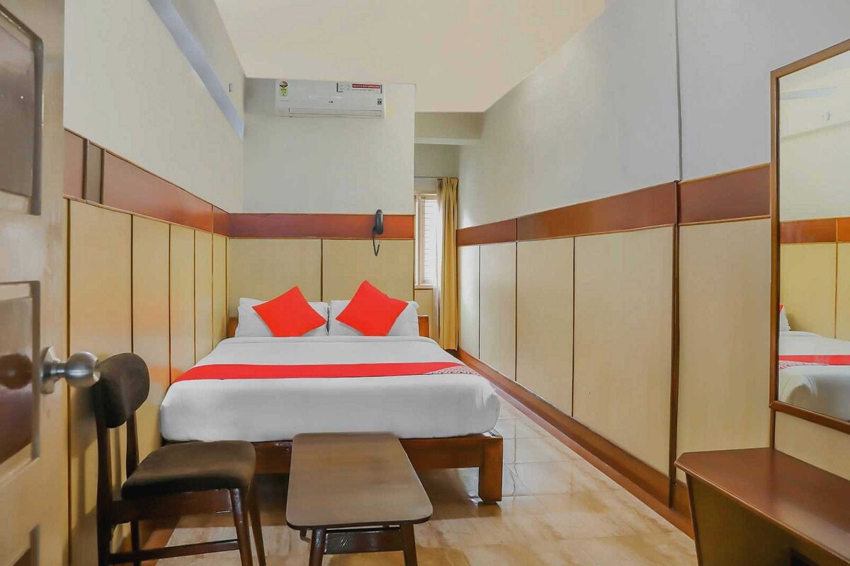 Una habitación de hotel con cama, mesita de noche, silla y espejo.