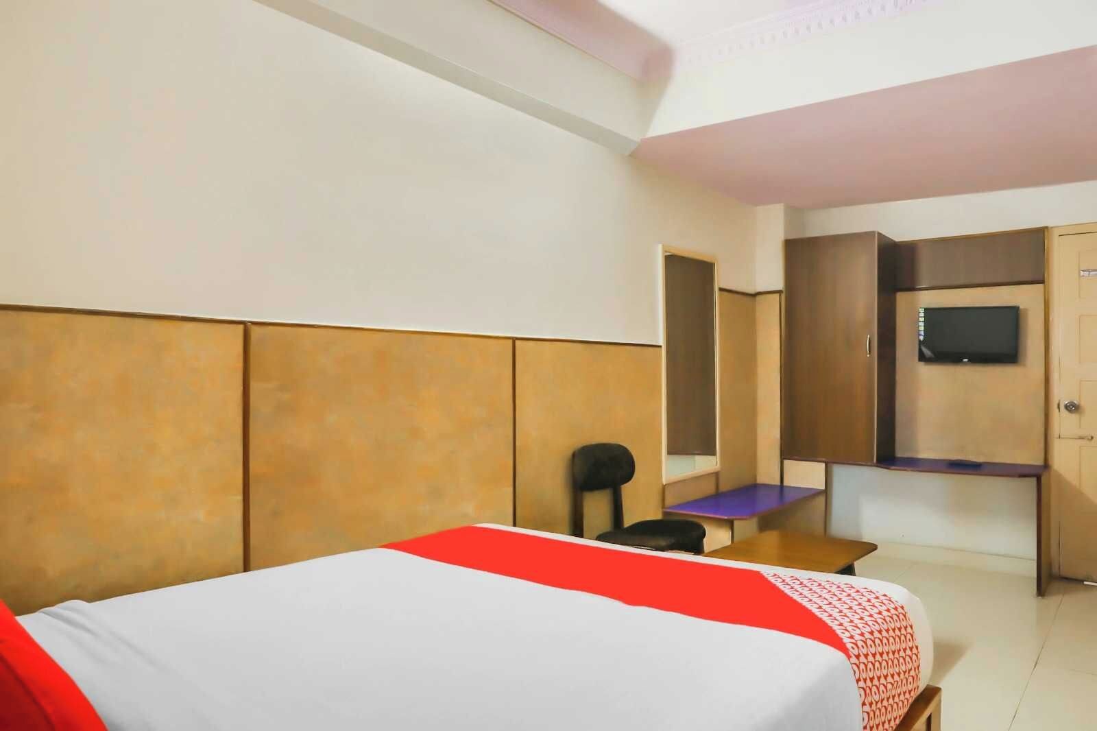 A hotel room with a bed, a desk, a chair, a television, and a wardrobe.