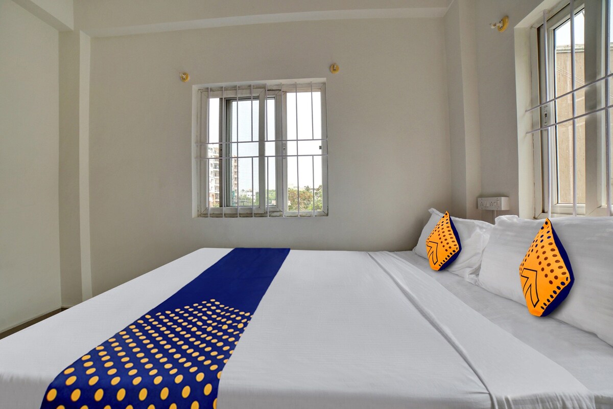 Habitación de hotel con una cama grande, ventana con persianas y vistas a edificios.
