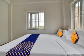 Habitación de hotel con una cama grande, ventana con persianas y vistas a edificios.
