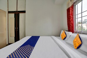 Habitación de hotel con cama, ventana con cortinas rojas y vistas a edificios.