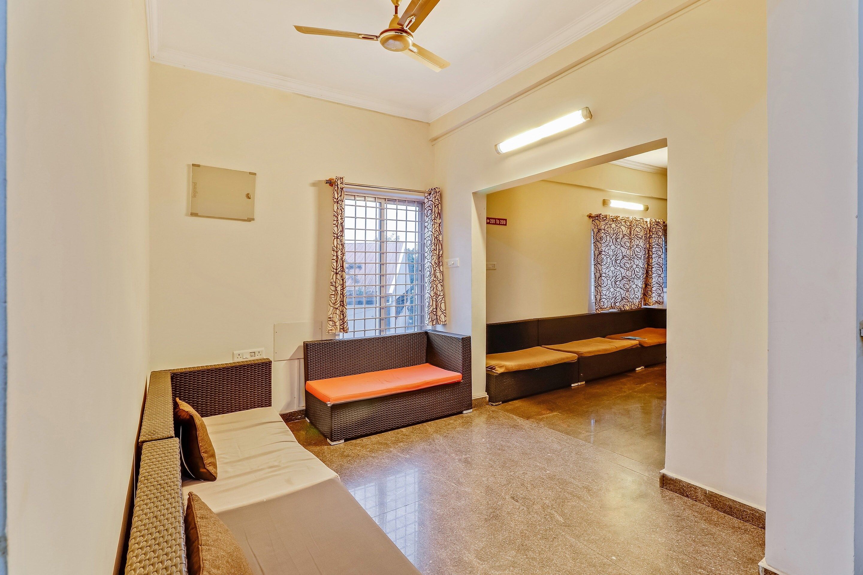 Habitación de hotel con sofá, cama, ventilador de techo y ventana con cortinas estampadas.