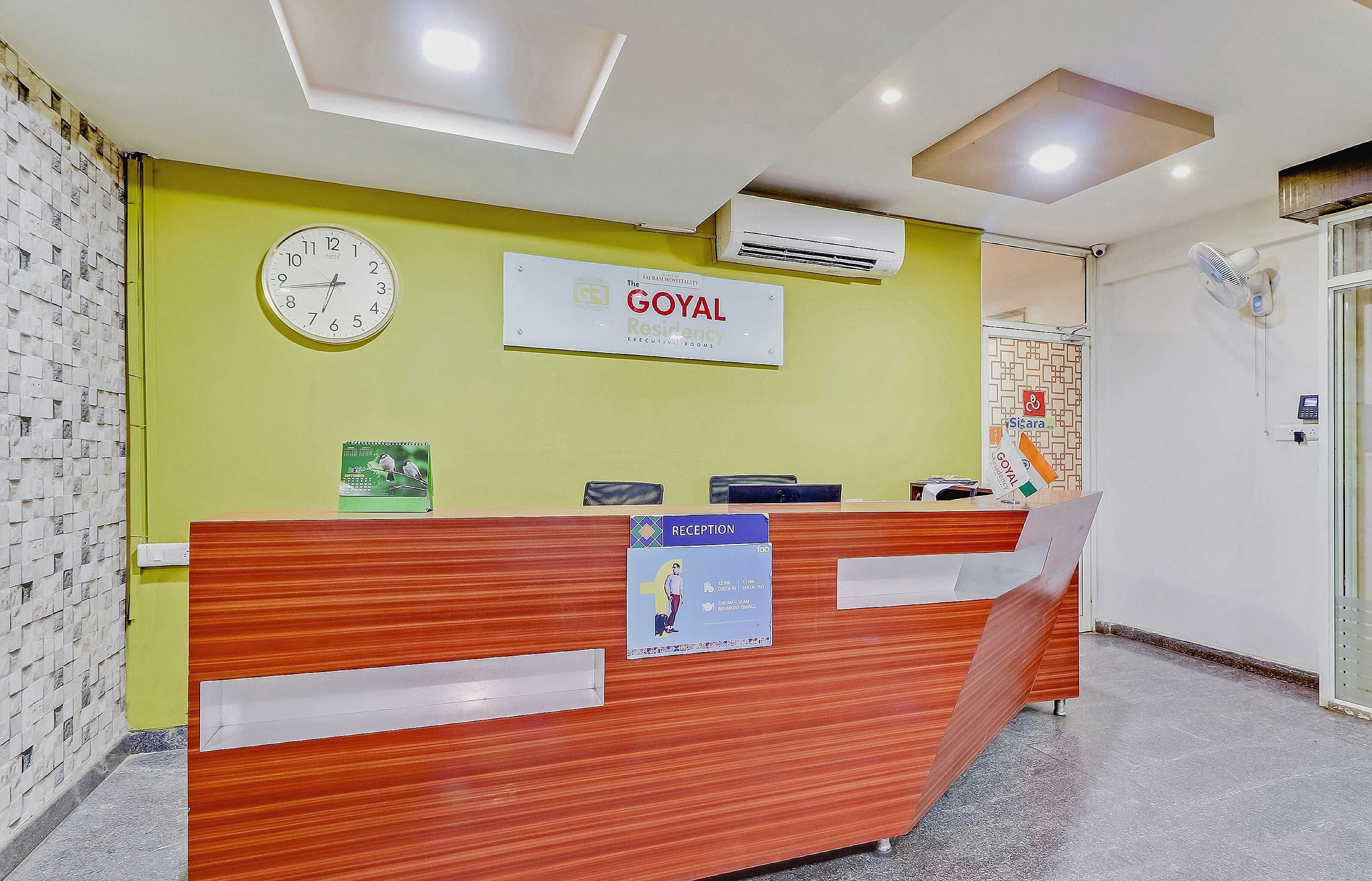 A reception desk with a clock, a sign for 'GOYAL Residency Executive Rooms,' and a reception area with a reception counter.
