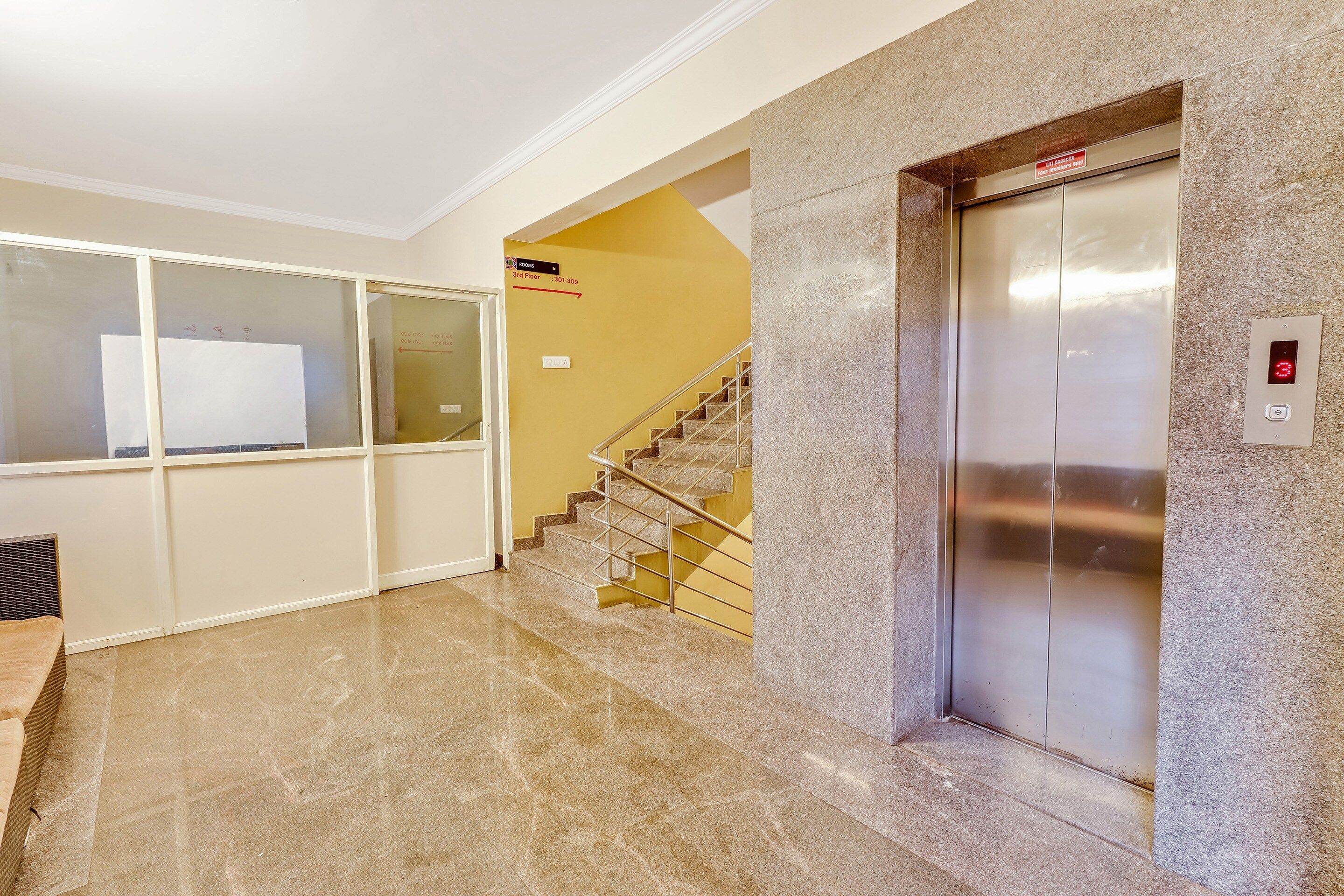 Un vestíbulo de hotel con piso de mármol, un ascensor y una escalera que sube al tercer piso.