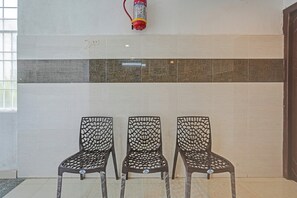 Three chairs with a web-like pattern, a fire extinguisher mounted on the wall, and a tiled floor with a decorative strip. - Hotel O Sri Ranga Boarding & Lodging (Bangalore)