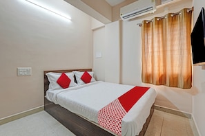 Habitación de hotel con cama, enchufe, unidad de aire acondicionado y ventana con cortinas.