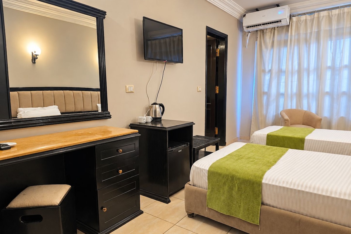 A hotel room with a bed, a desk with a chair, a television, and an air conditioning unit.