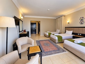A hotel room with a sofa, two single beds, a desk, and a large rug. - Davinci Beach Hotel (Red Sea Governorate)