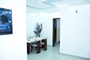 Un área de comedor con una mesa, sillas, una planta en maceta y una pared blanca con un accesorio de iluminación.