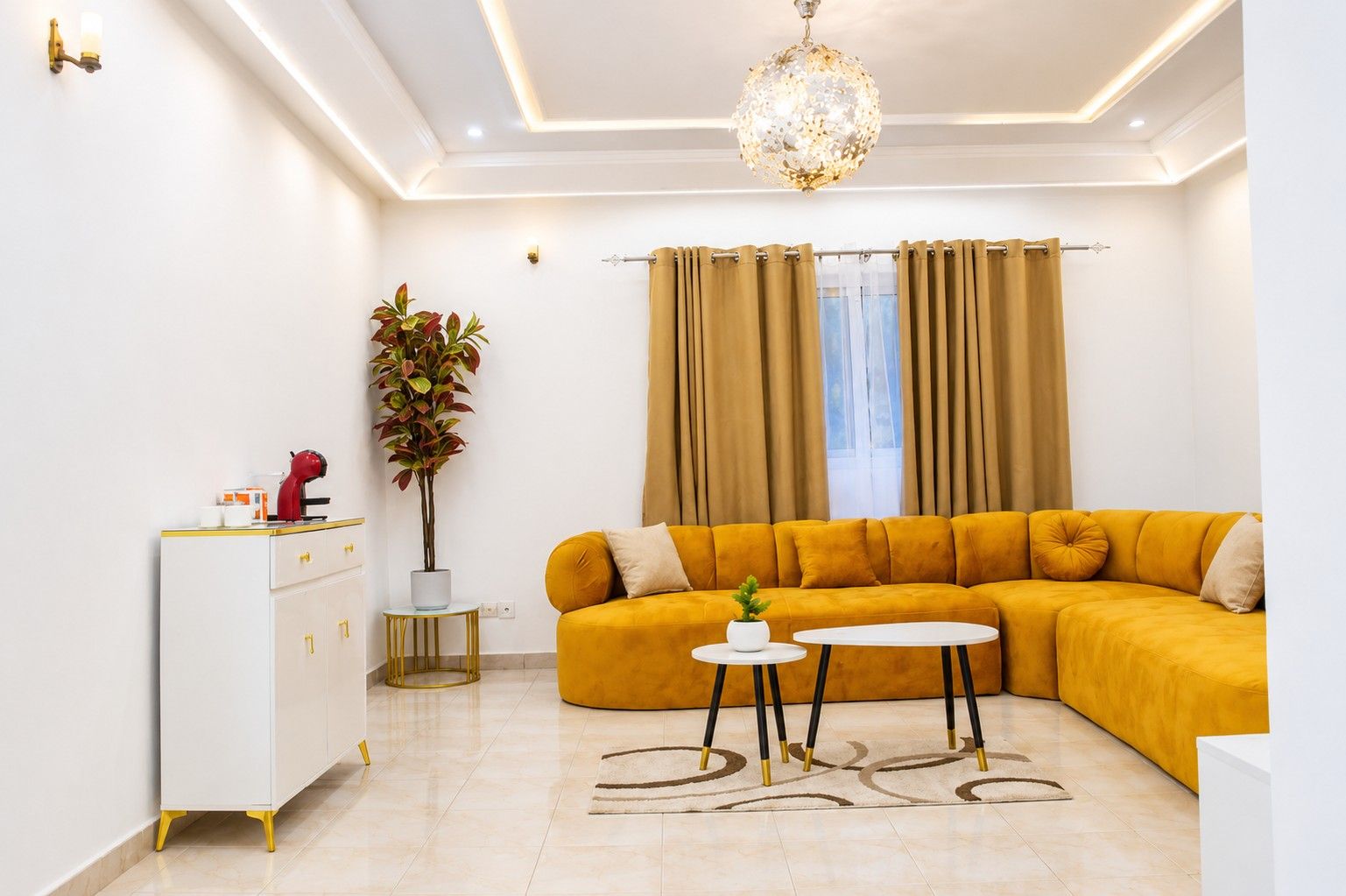 A modern living room with a sectional sofa, a small round table, a cabinet, and a potted plant.