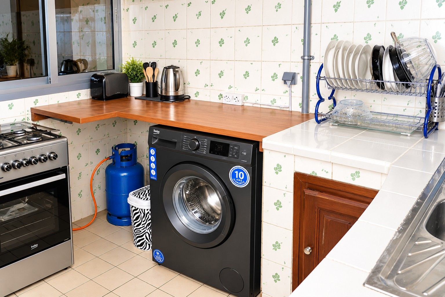 A compact kitchen with a gas stove, a washing machine, and a dish rack.