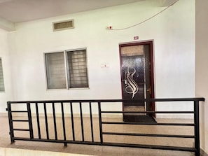 Passadís amb barana de metall negre, una porta amb un panell de vidre decoratiu i una finestra amb reixatge metàl·lic.