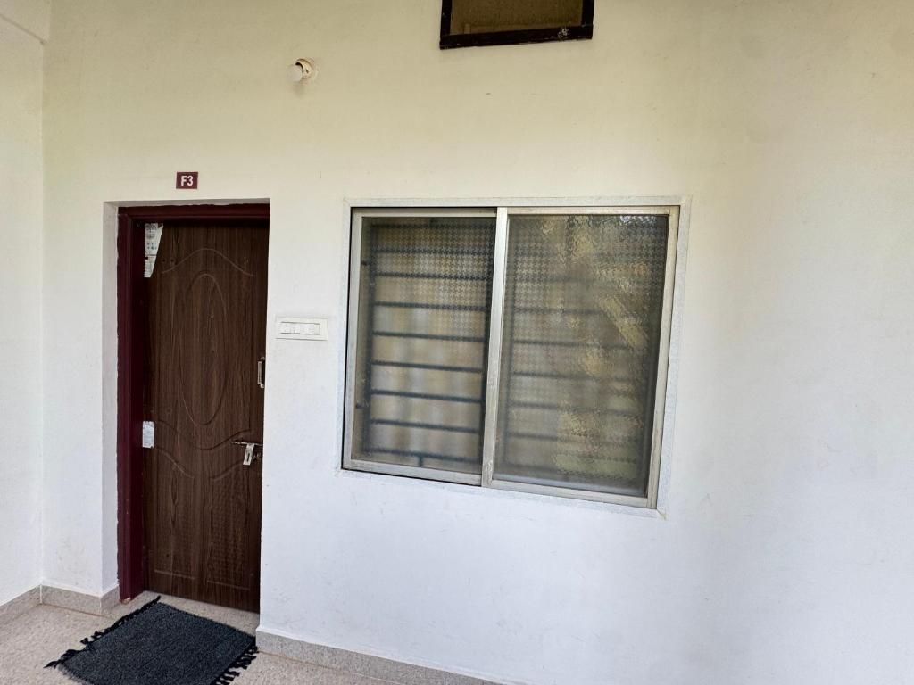 Una habitación con puerta de madera, ventana con reja de metal y una pequeña lámpara fijada a la pared.