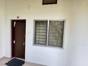 Una habitació amb una porta de fusta, una finestra amb reixatge metàl·lic i una petita làmpada fixada a la paret.