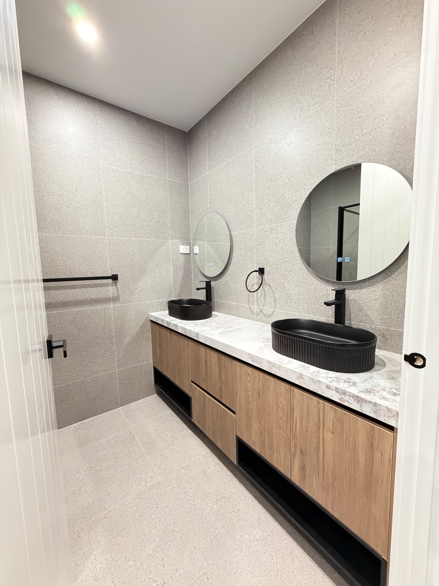 A modern bathroom with a wooden vanity, two sinks, and a shower area.