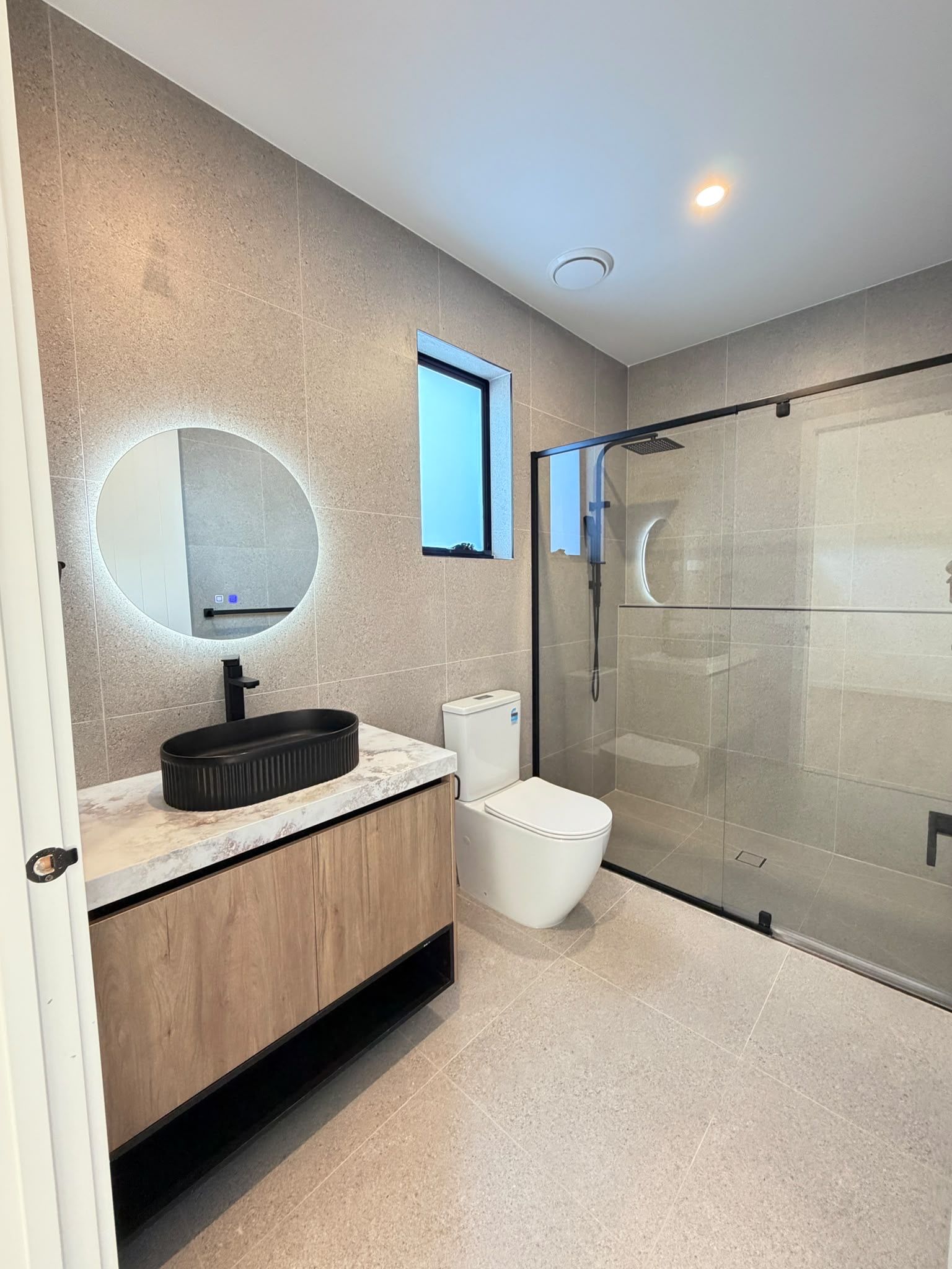 Un baño moderno con un espejo redondo, un inodoro y una ducha con cerramiento de vidrio.