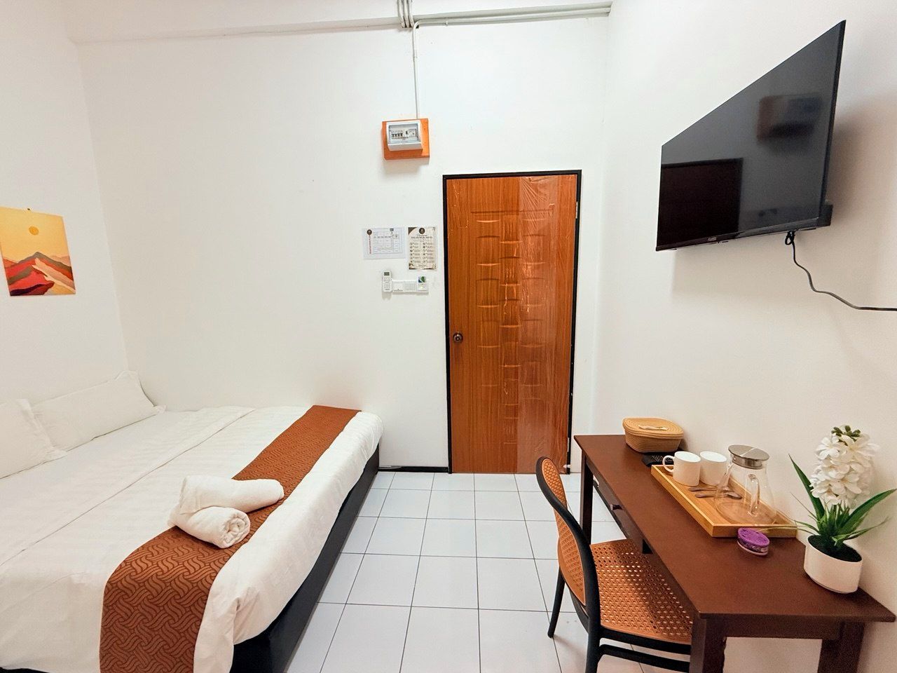 Une chambre d’hôtel avec un lit, un bureau avec un plateau, une plante en pot et un téléviseur fixé au mur.