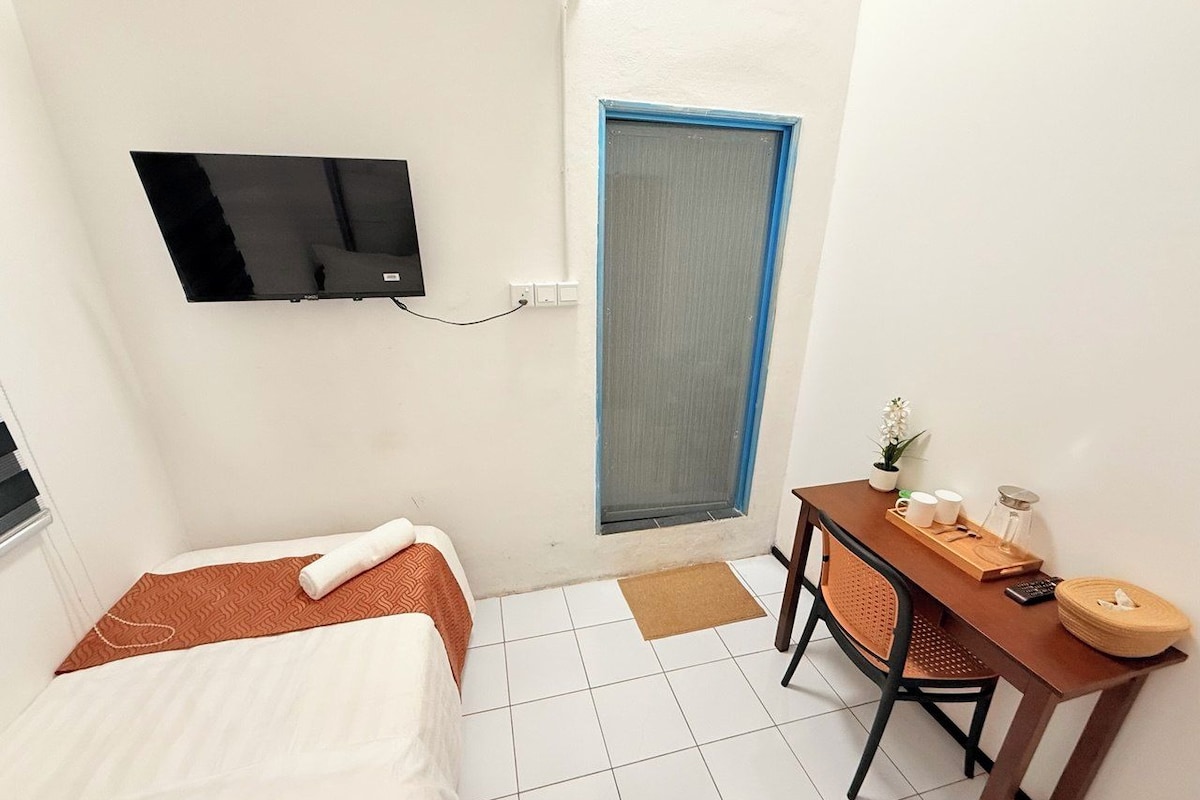 A compact hotel room with a bed, a desk, a chair, a television, and a door.