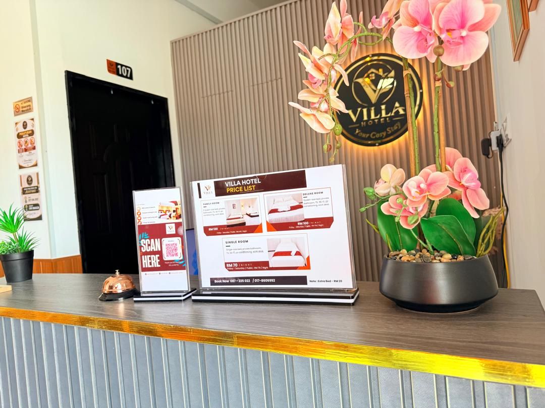 Ein Hotelrezeptionstresen mit einer digitalen Preisliste, einem Topf mit einer Orchidee und einem Schild für Zimmer 107.