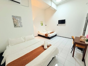 A hotel room with two beds, a dining table with chairs, and a flat-screen TV mounted on the wall.