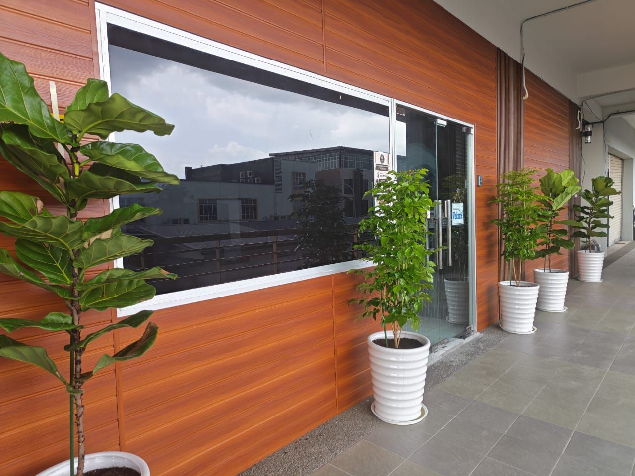 A modern building exterior with a large window, potted plants, and a tiled floor.