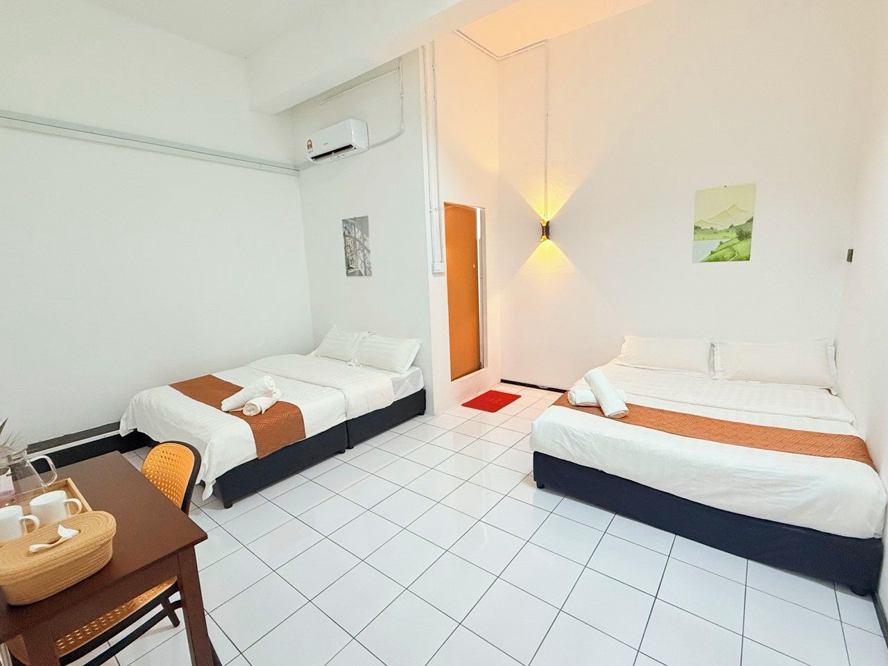 Habitación de hotel con dos camas, una mesa de comedor y una lámpara fijada a la pared.