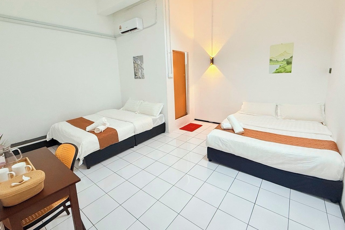 A hotel room with two beds, a dining table, and a wall-mounted light fixture.