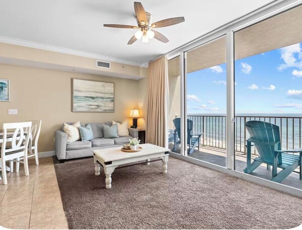 Ein Balkon mit Blick auf das Meer, ein Deckenventilator, eine Couch, ein Couchtisch und ein Essbereich mit Stühlen.