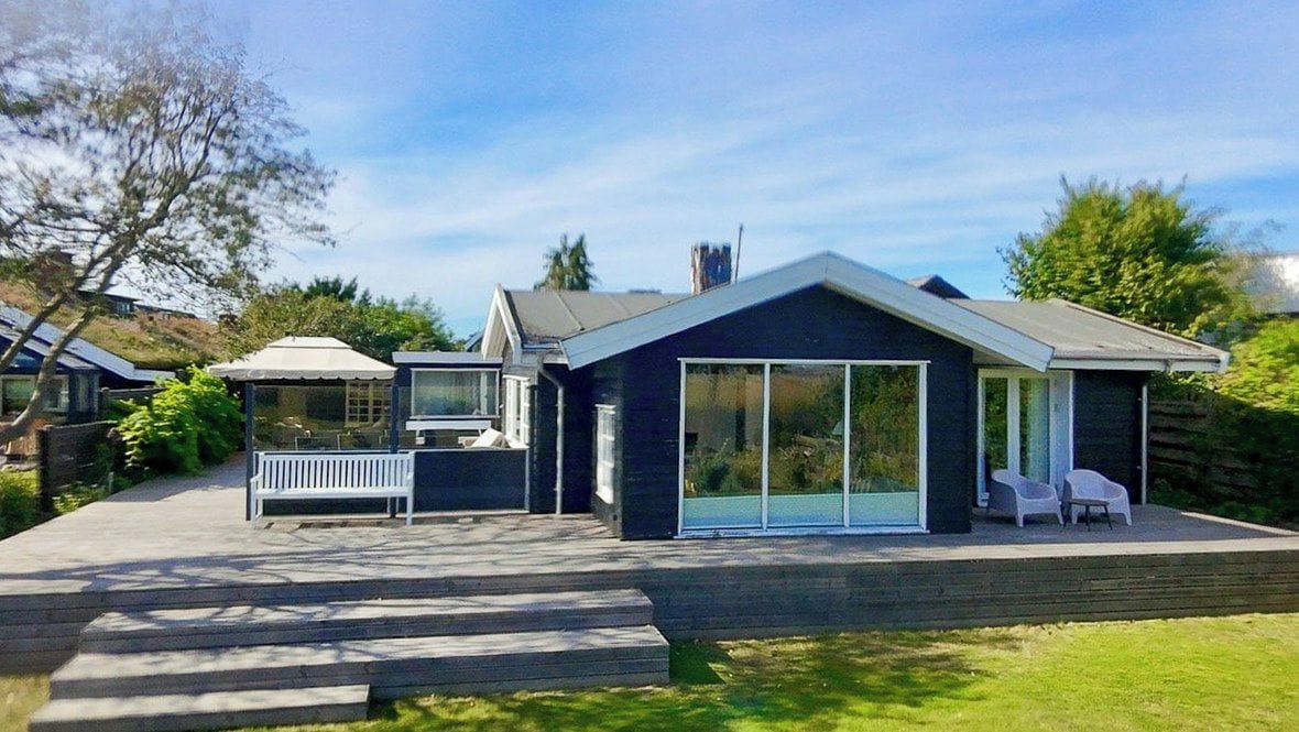 Una casa moderna con un amplio ventanal, un patio con un banco y una pequeña zona de estar al aire libre.