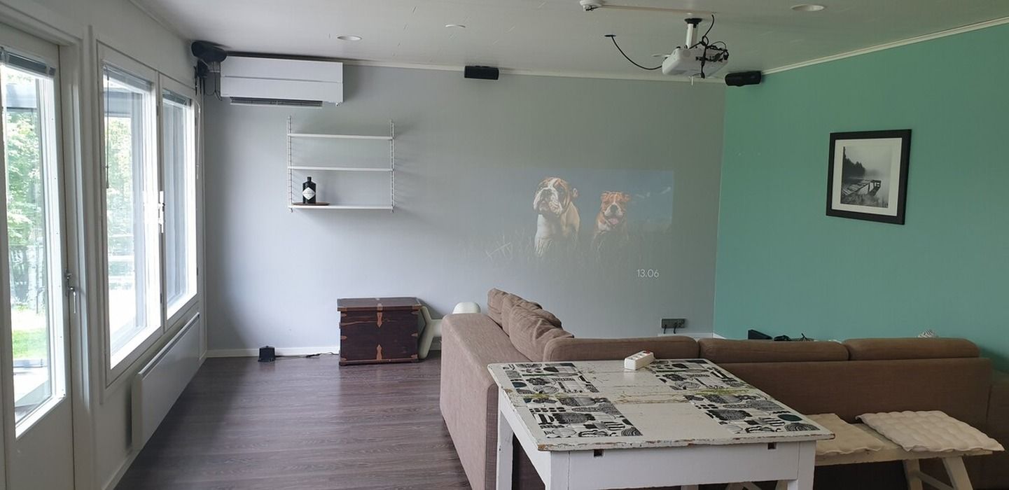 Un salon comprenant un canapé, une table basse avec un magazine, un écran de projection et une étagère fixée au mur.
