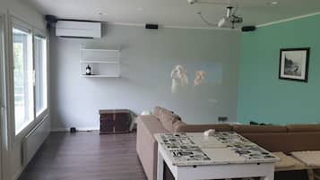 Un salon comprenant un canapé, une table basse avec un magazine, un écran de projection et une étagère fixée au mur.