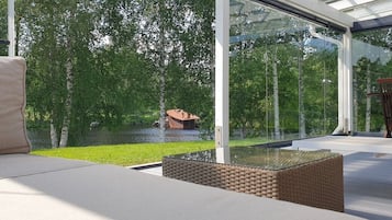 Un espacio moderno con asientos al aire libre, una estructura de vidrio, una mesa de mimbre y vistas a un paisaje natural.