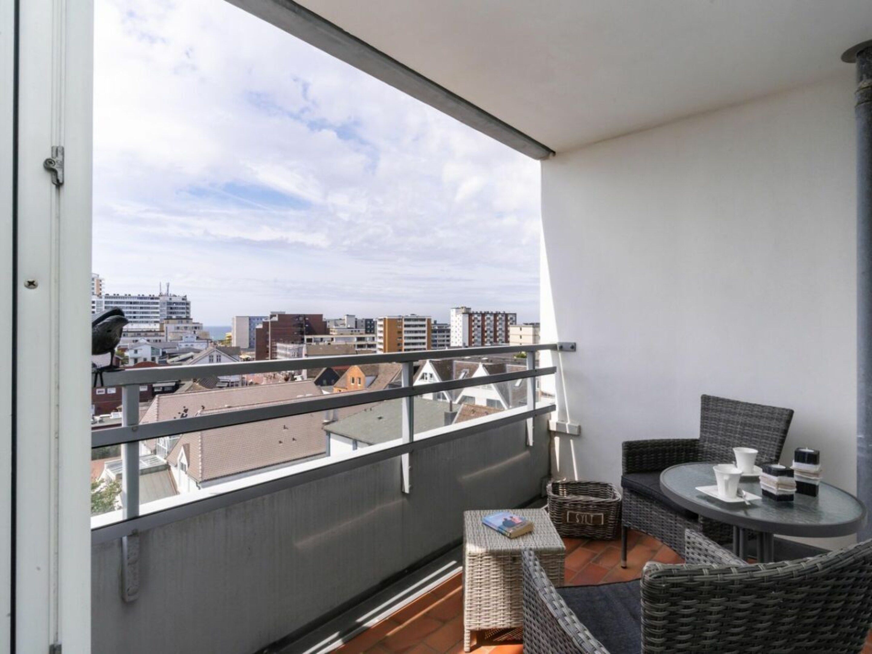 A balcony with wicker furniture, a small table, and a view of the cityscape.